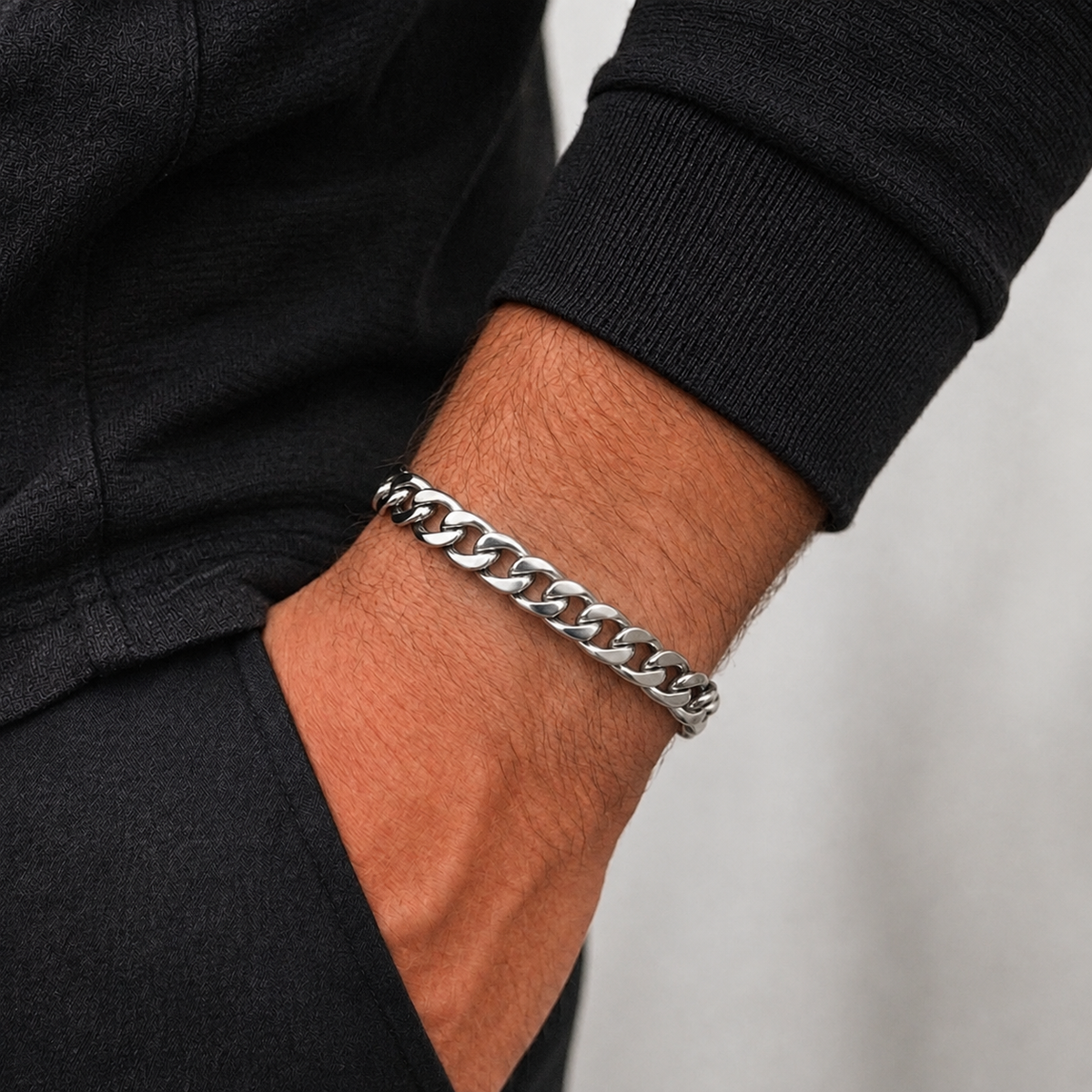 A close-up of a person's wrist wearing a thick silver Cuban link chain bracelet, paired with a black long-sleeve top.